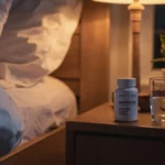 Bottle of magnesium supplements on a nightstand next to a glass of water in a calming bedroom setting, symbolizing natural sleep aid.