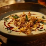 Bowl of creamy Kashk-e Bademjan garnished with mint and fried onion, served with flatbread