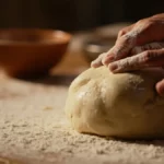 Hands kneading fresh, healthy homemade pizza dough on a wooden board ready for rising